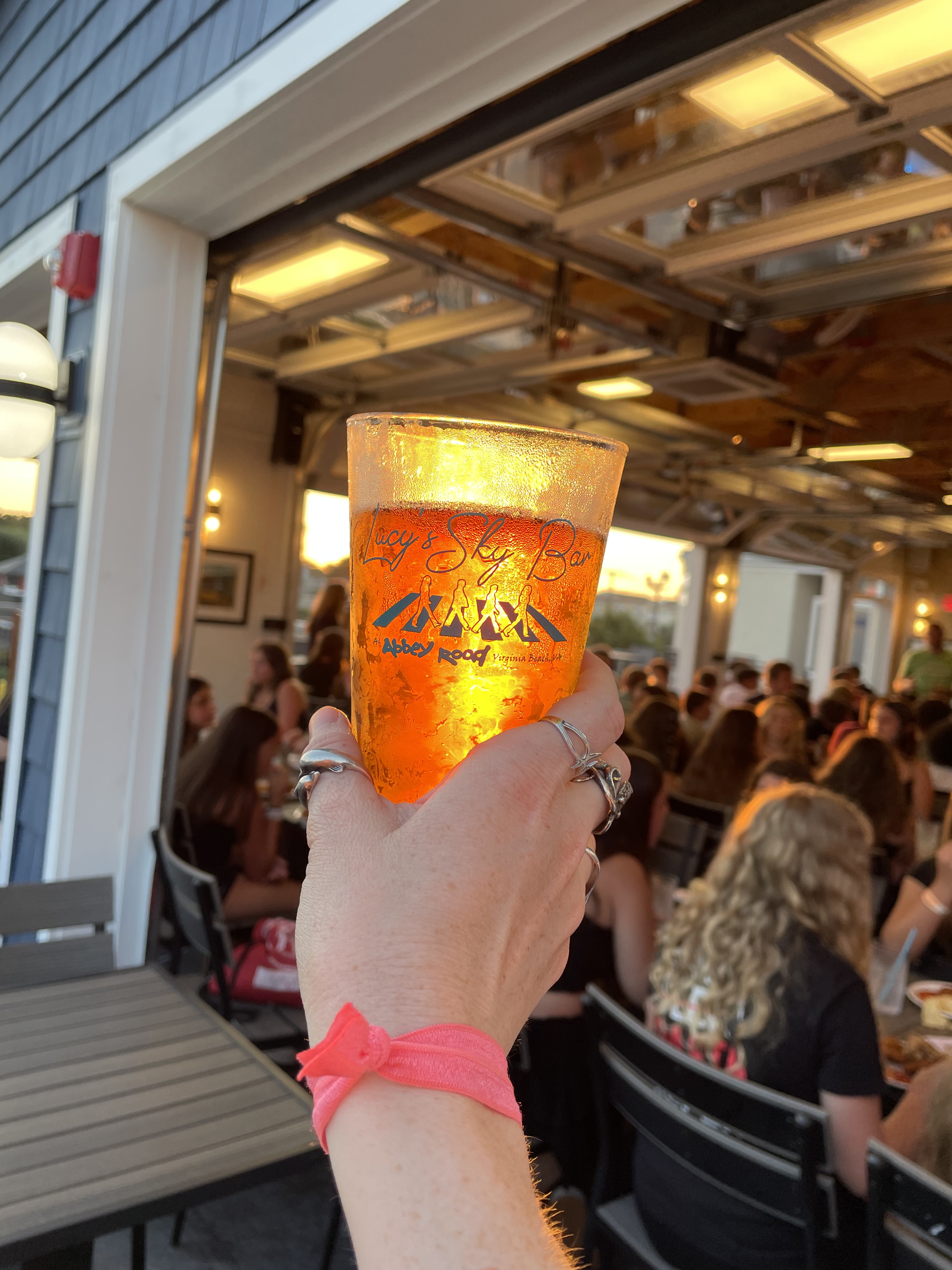 A beer glass with the sun shining through, a crowd of people in the background at Lucy's Sky Bar in Virginia Beach