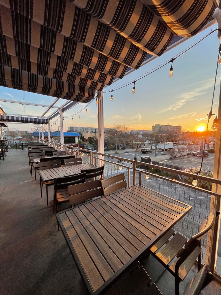 Lucy's Sky Bar patio with a beautiful sunset view, spacious seating, and string lights